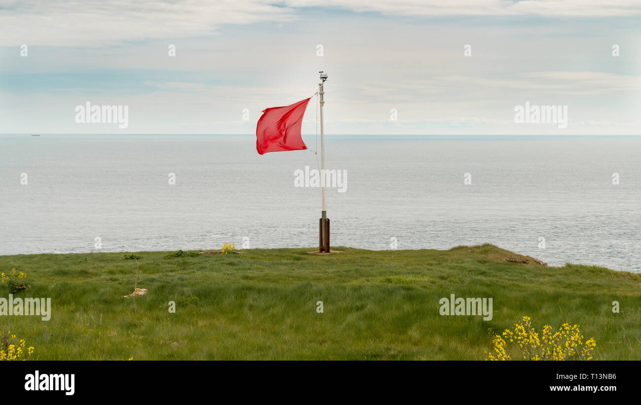 Red flag in the wind, seen on the South West Coast Path near Emmett's Hill, Jurassic Coast, Dorset, UK Stock Photo