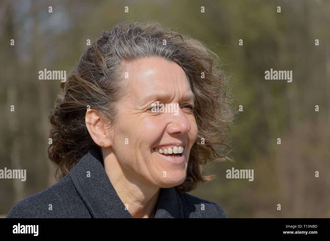 Smiling friendly woman with tousled hair standing on a bridge in the countryside in spring sunshine Stock Photo