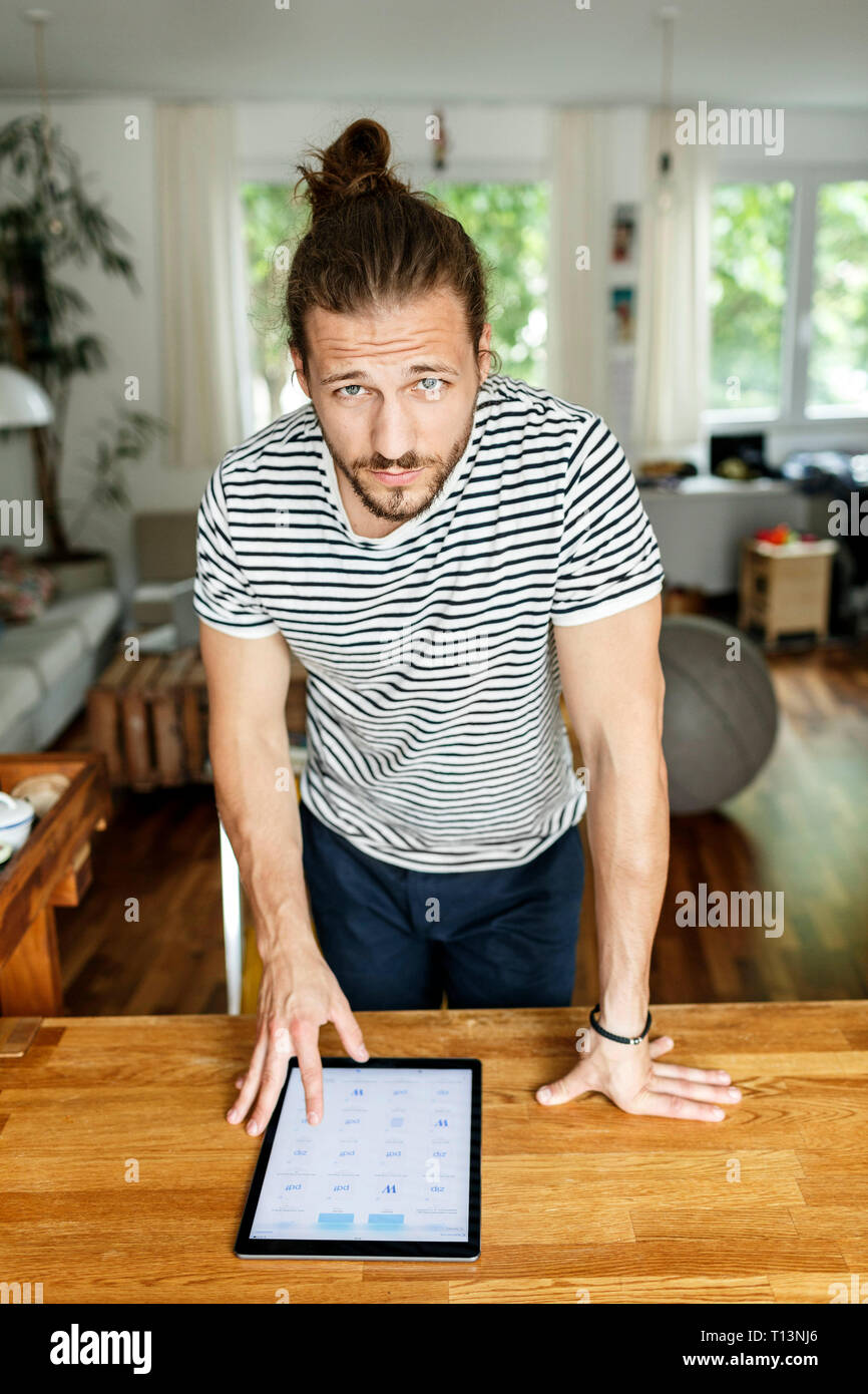 Young man with a bun standing at table, using digital tablet Stock Photo