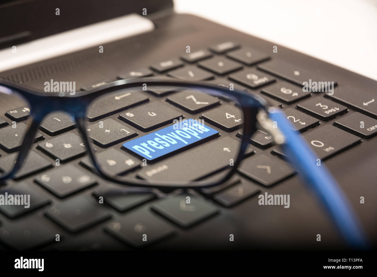 View of the PC keyboard through the lens of the glasses on the button with the written Presbyopia Stock Photo