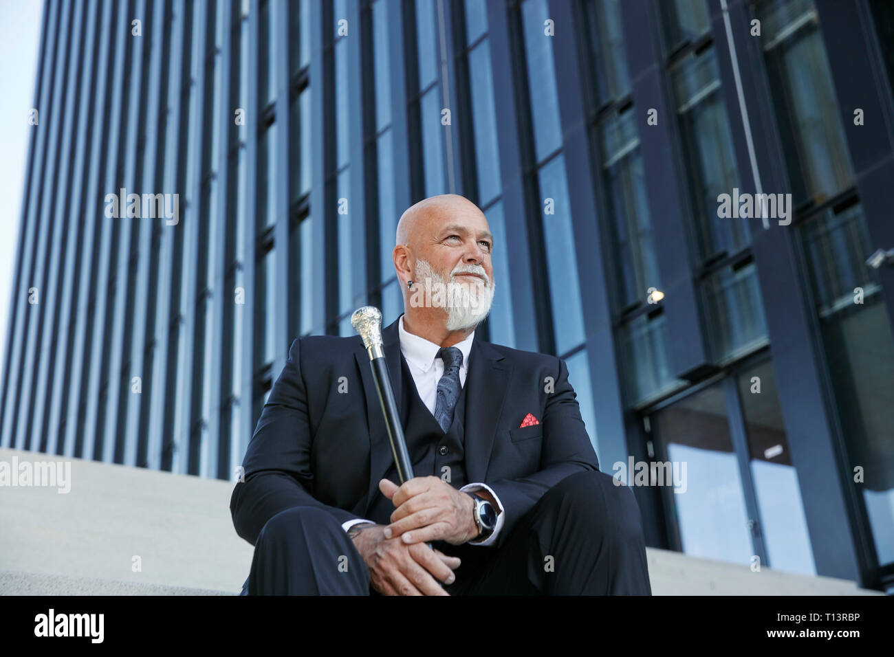 Elegant businessman with walking cane, sitting on stairs in the city Stock Photo