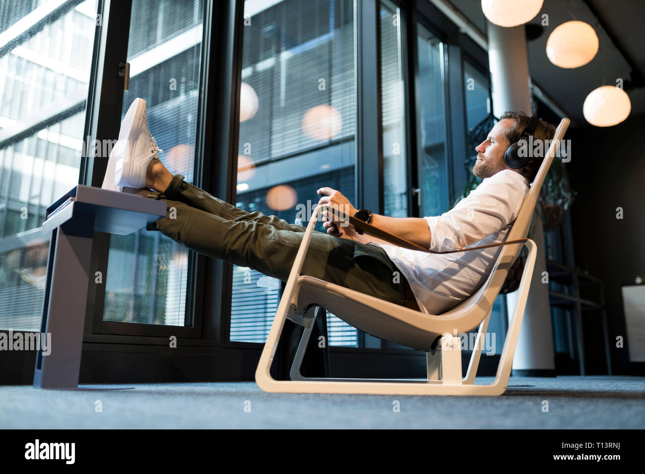 Casual businessman relaxing in lounge area of a coworking space, listening music Stock Photo