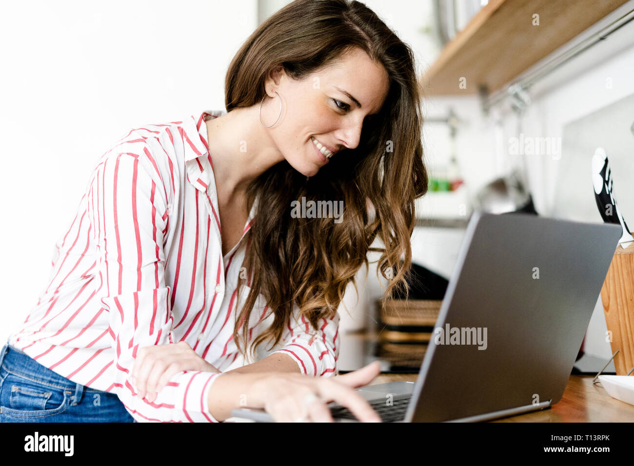 Smiling woman using laptop in kitchen at home Stock Photo