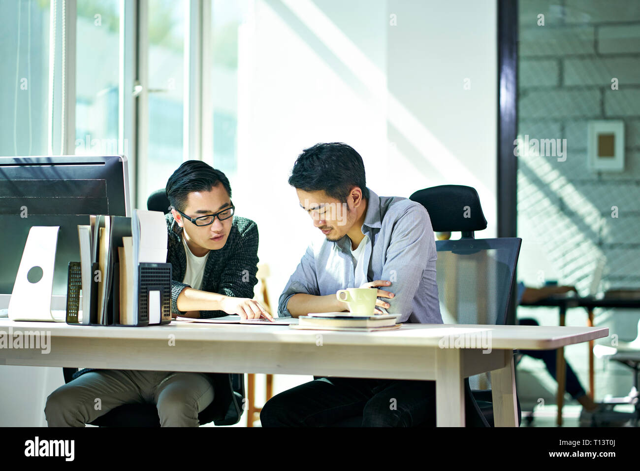 two young asian corporate executives working together discussing business plan in office. Stock Photo