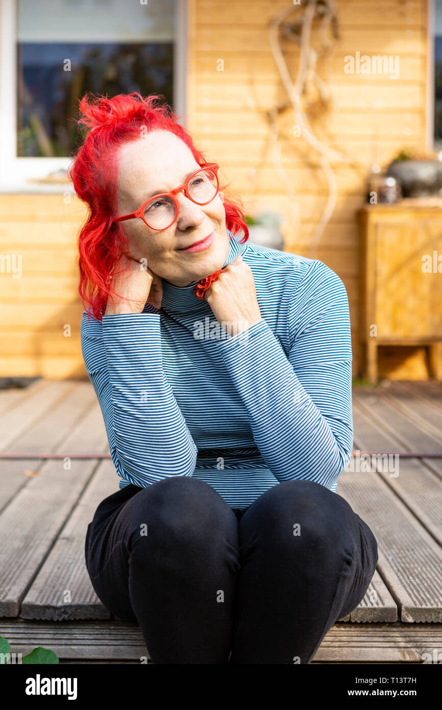Portrait Of Smiling Senior Woman With Red Dyed Hair Sitting On