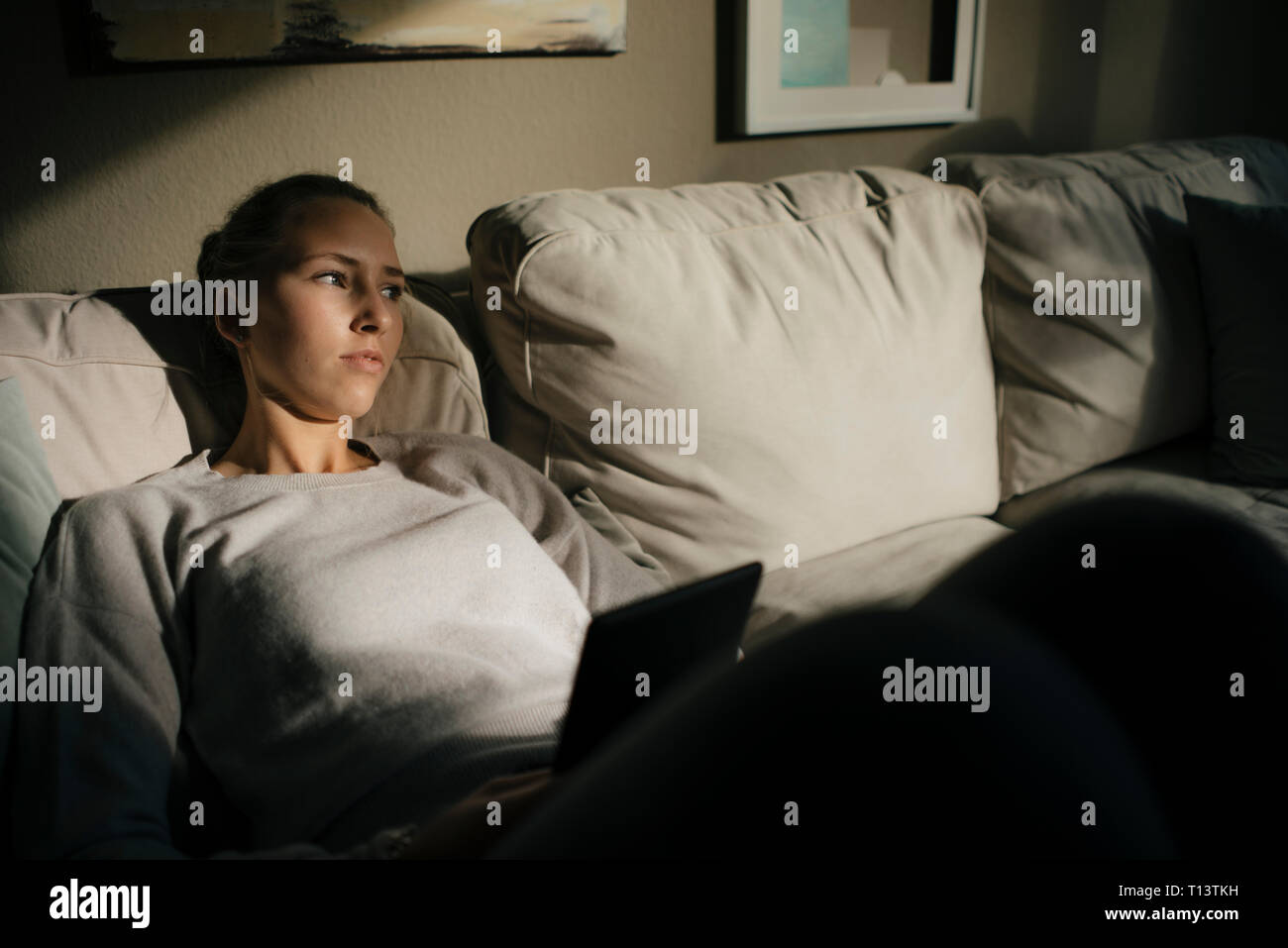 Serious teenage girl with tablet sitting on couch at home Stock Photo ...