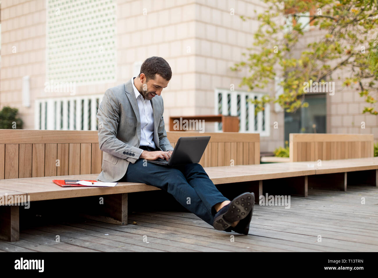 Smiling businessman sitting on a bench using laptop Stock Photo