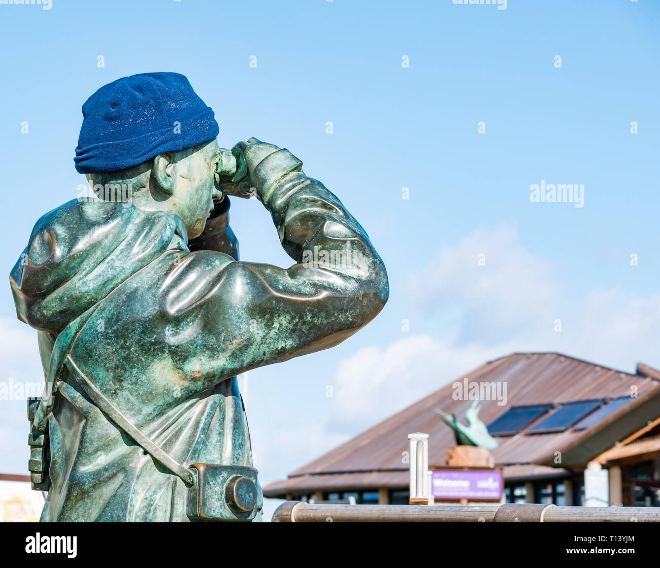 North Berwick, East Lothian, Scotland, UK, 23rd March 2019. UK Weather: Sunny Spring weather at the seaside town. Bronze statue called The Watcher by Kenny Hunter with a warm hat looking through binoculars Stock Photo