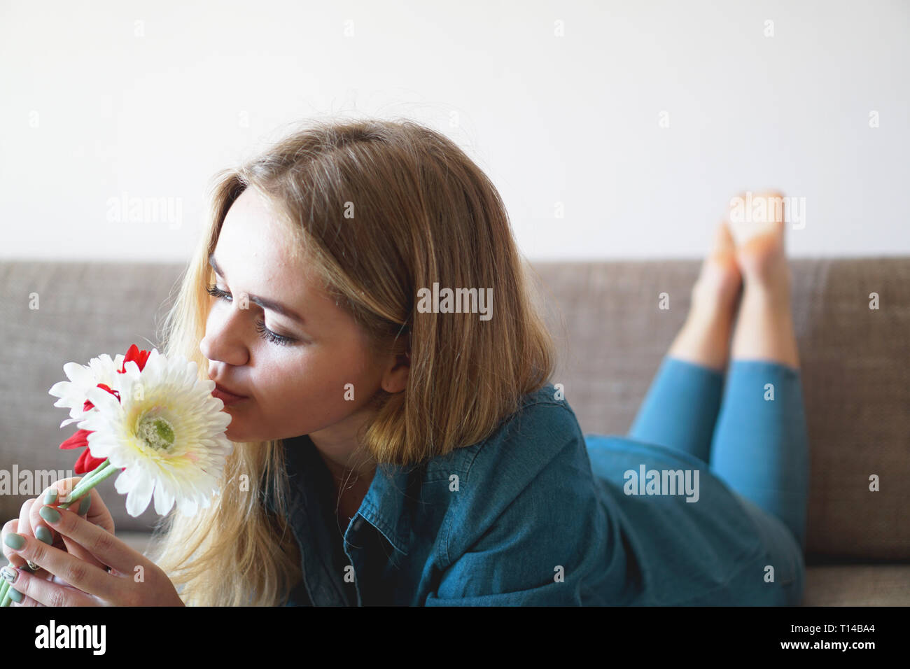 Attractive young woman sniffing bouquet of flowers lying on the couch Stock Photo