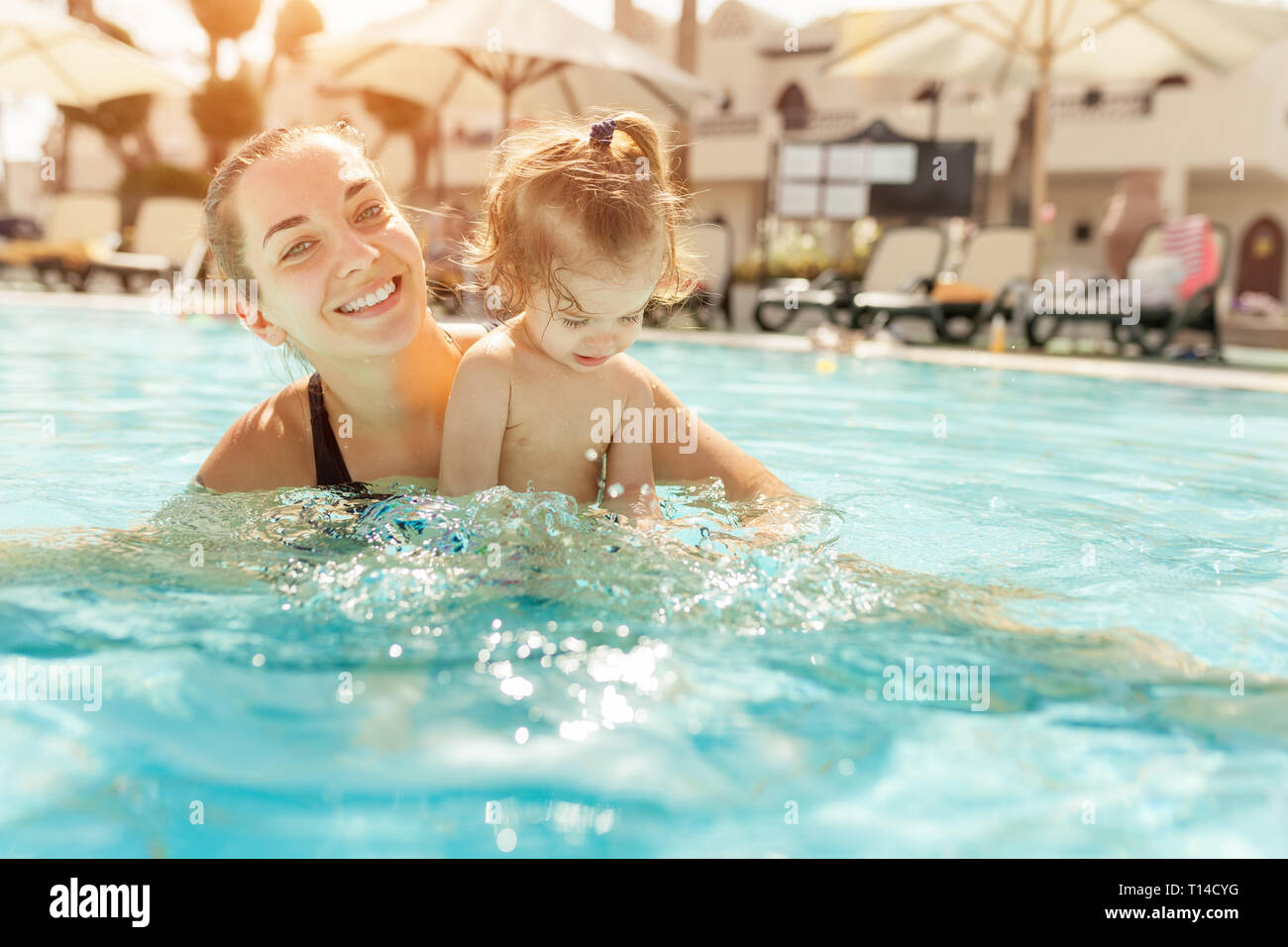 Mom and little daughter are played in the open swimming pool. Family