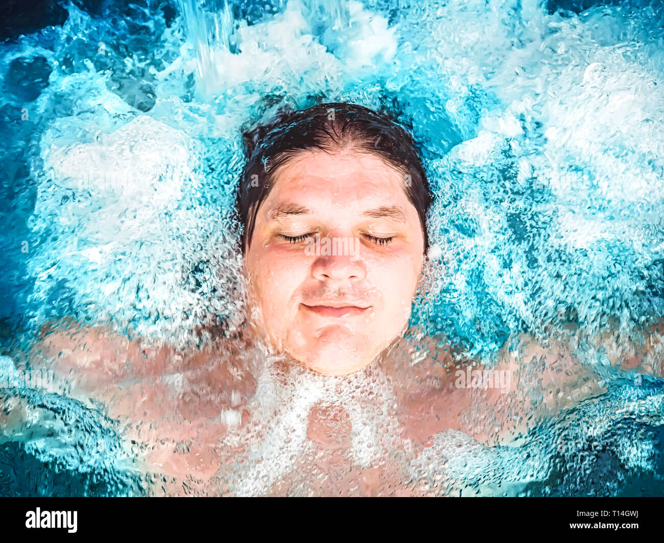 Happy man relaxing in the jacuzzi and closing his eyes. Caucasian boy resting in a pool lies in water. View from above. Swimming guy in a pool with Stock Photo