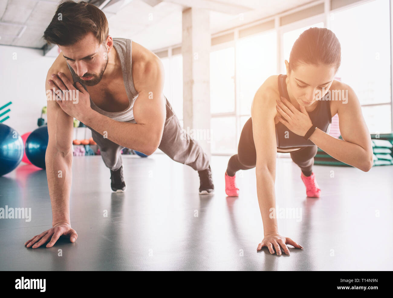 Slim girl and strong man are standing in one hand plank position and balancing on that hand. They look concentrated and concious. Stock Photo