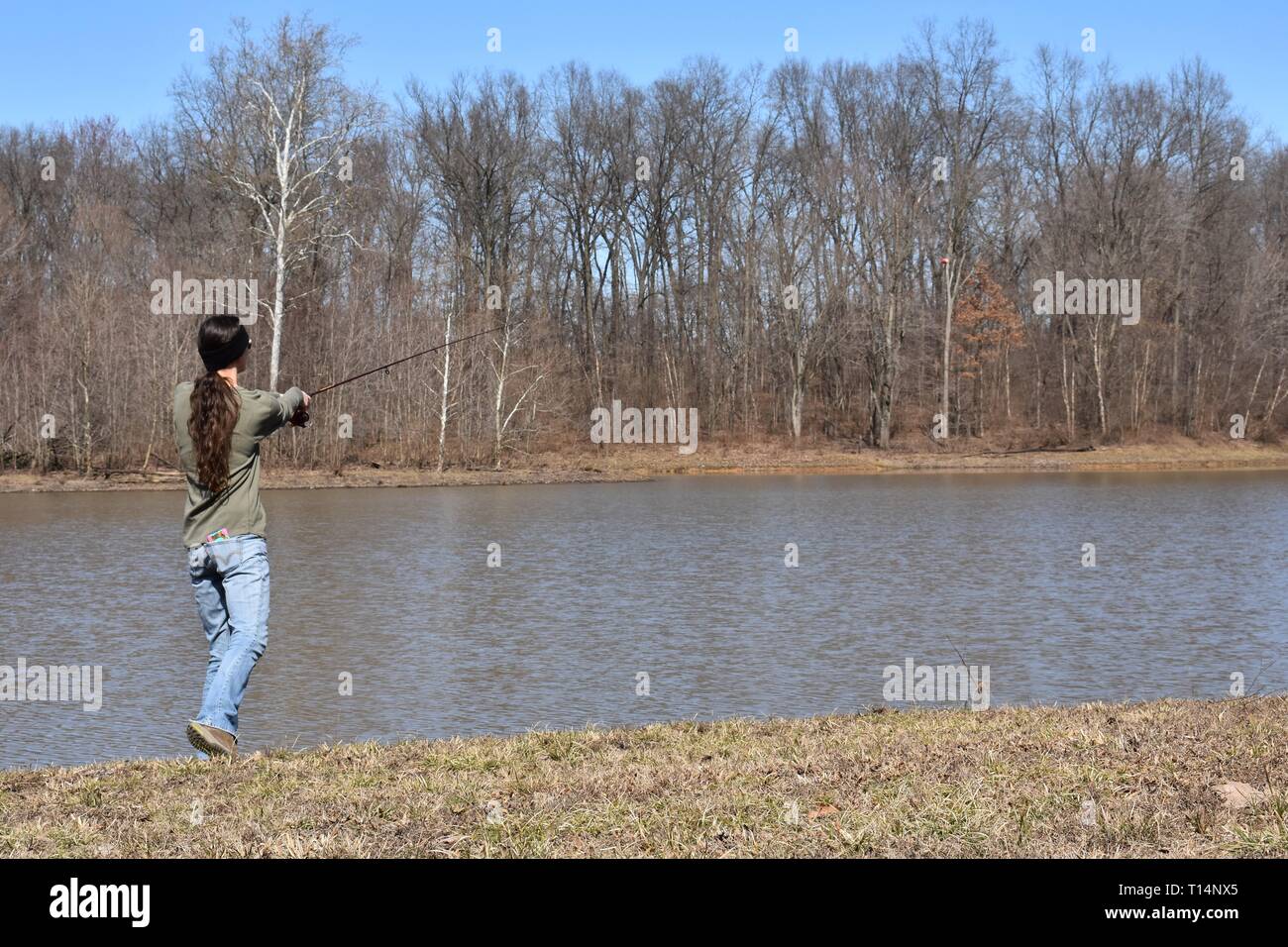Young woman casting a line into a lake from her fishing pole Stock Photo