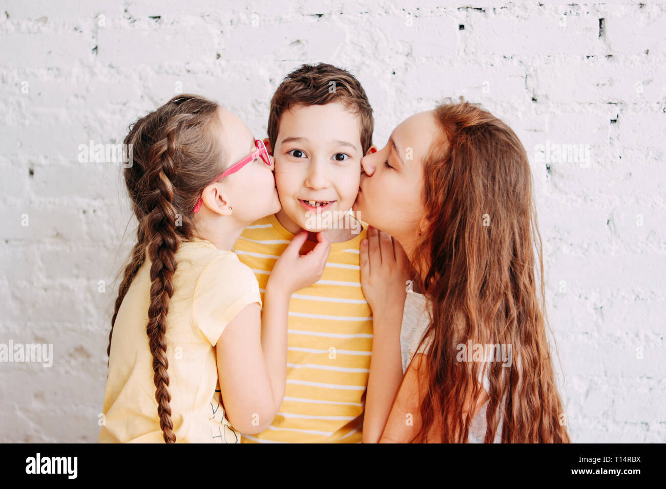 Girls sisters kissing boy brother with two sides isolated on white brick background Stock Photo
