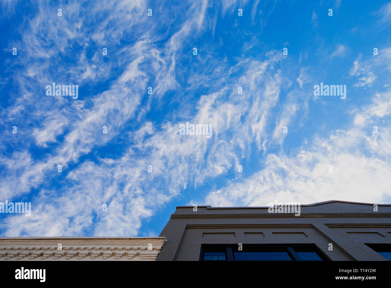 Cirrus clouds against a deep blue sky above old brick buidlings. Stock Photo