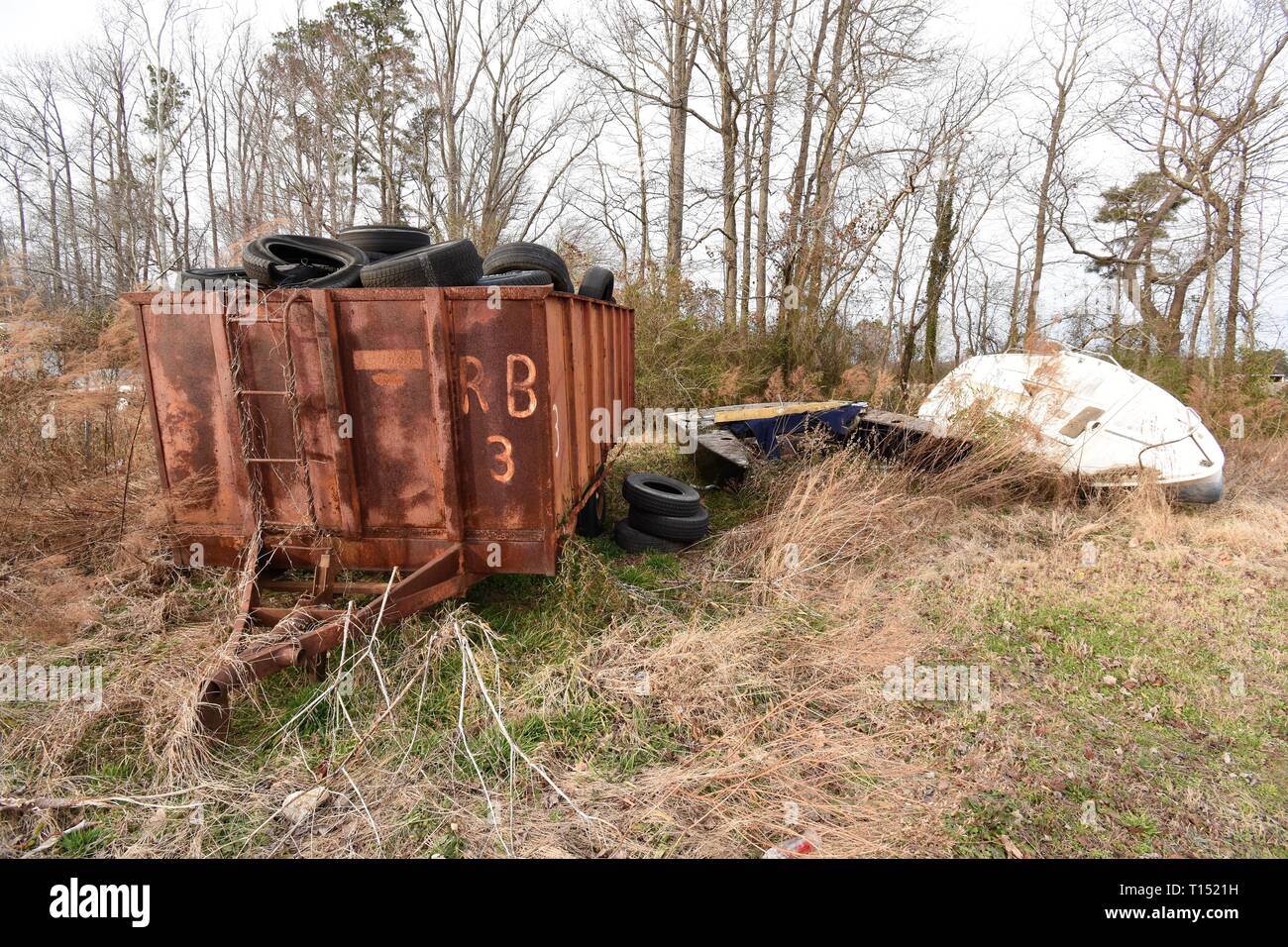Used and worn tires and overturned unseaworthy boat in overgrown yard in Maryland USA, the backyard of a home and business Stock Photo