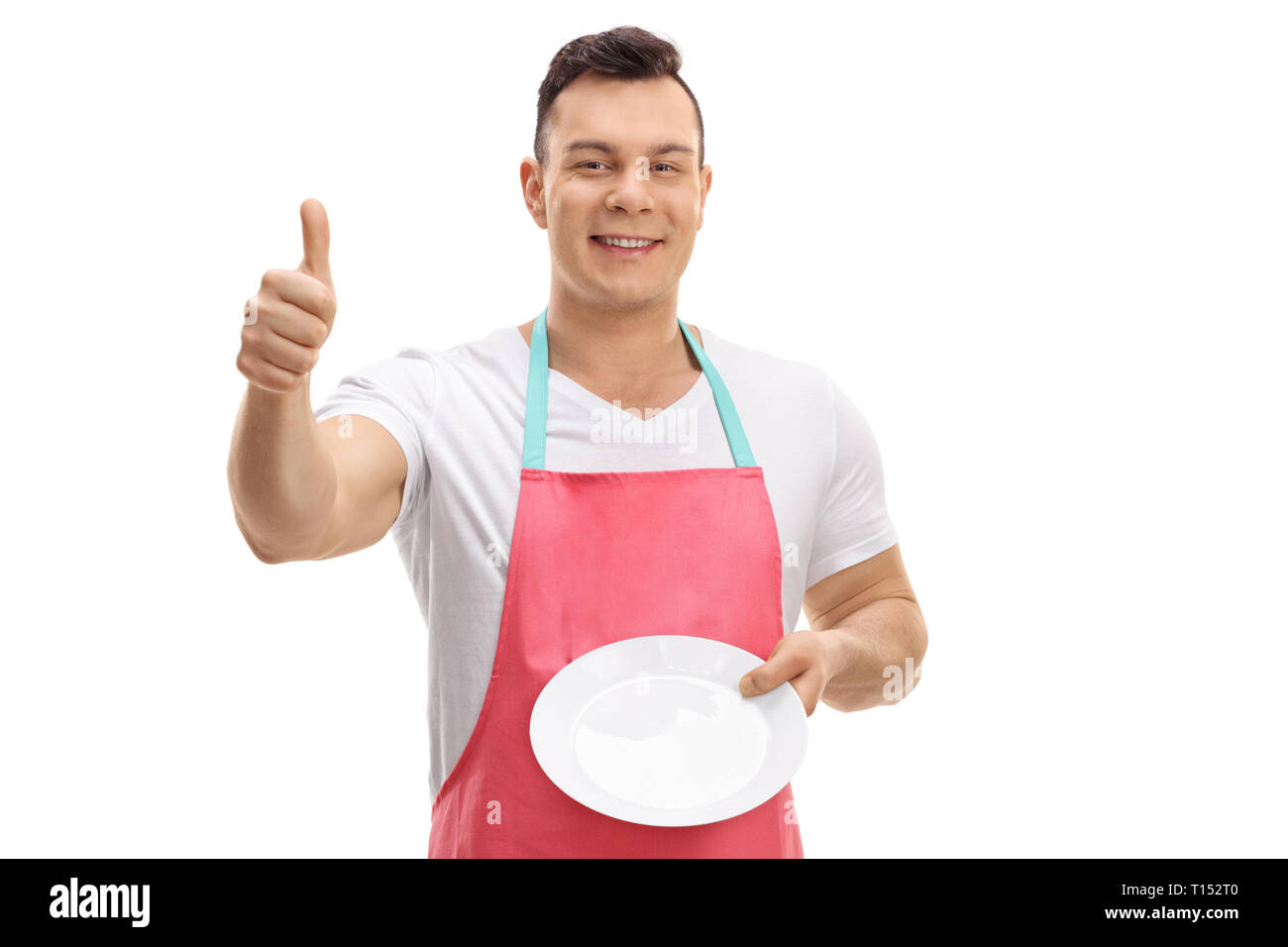 Young guy with an apron showing a clean plate and making a thumb up gesture isolated on white background Stock Photo