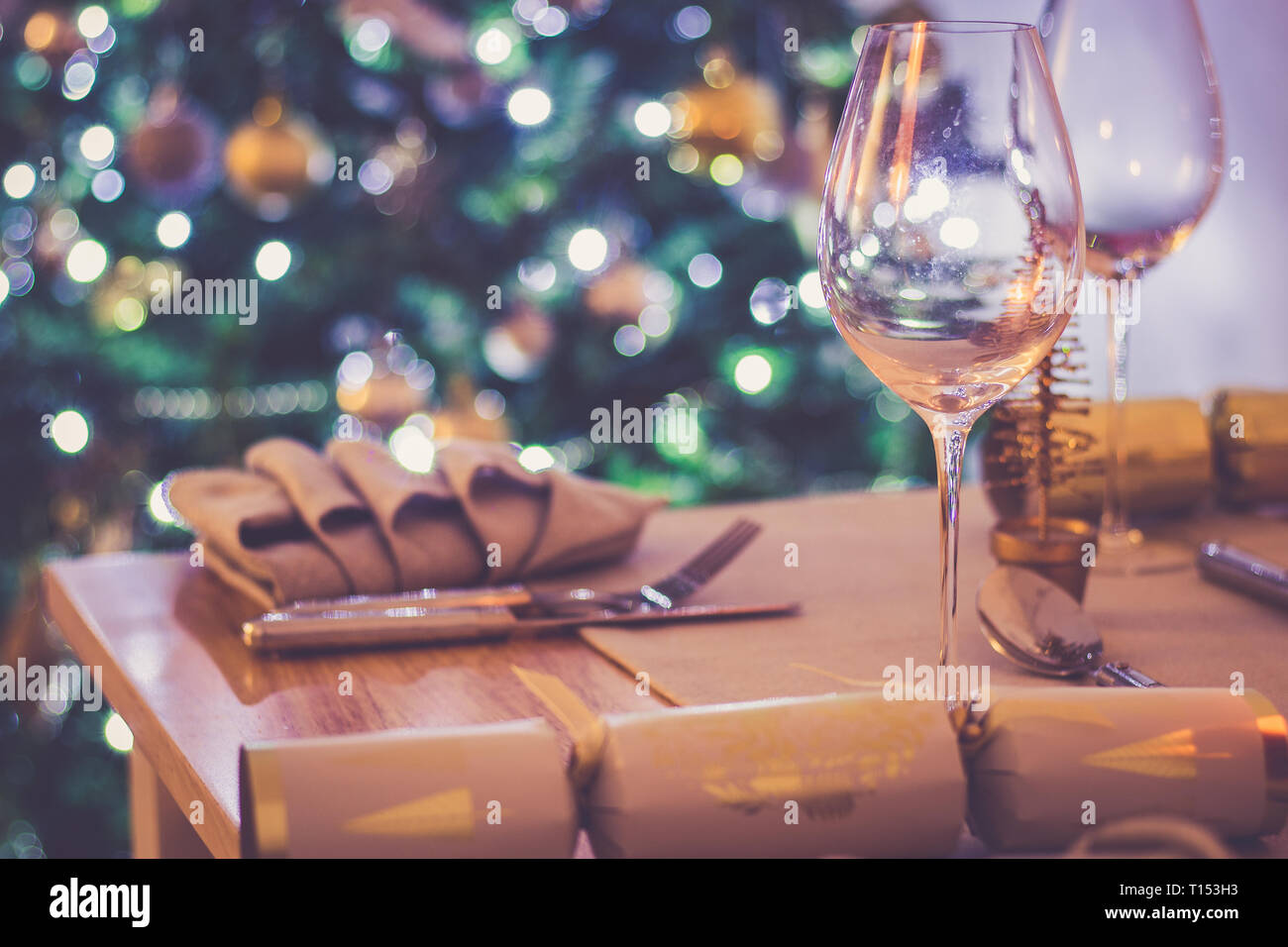 A dining table set for a Christmas meal, with defocussed tree light in the background Stock Photo