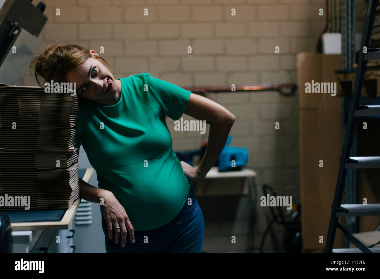Overwhelmed pregnant woman pulling funny faces in office cellar Stock Photo