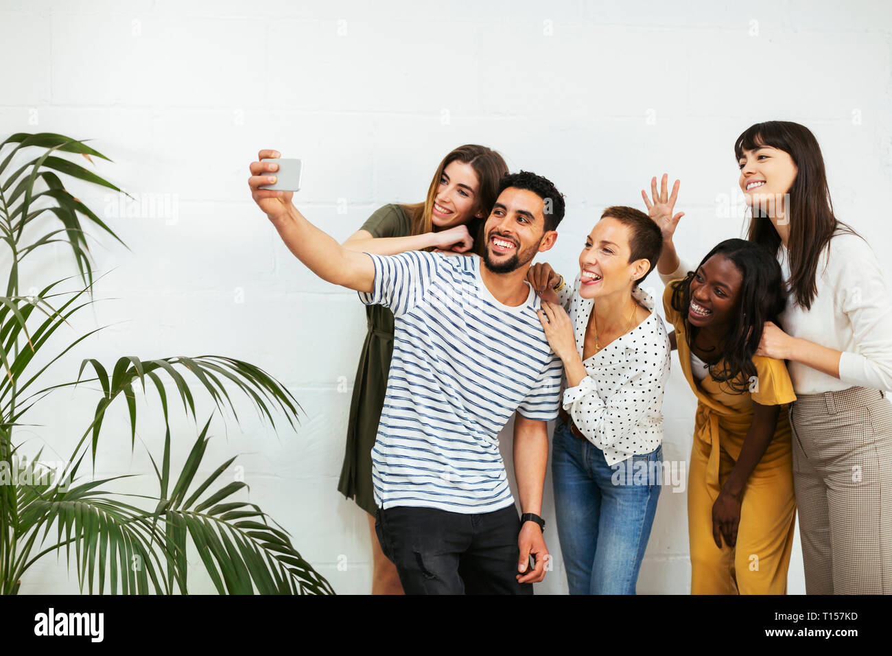 Playful colleagues standing at brick wall taking a selfie Stock Photo