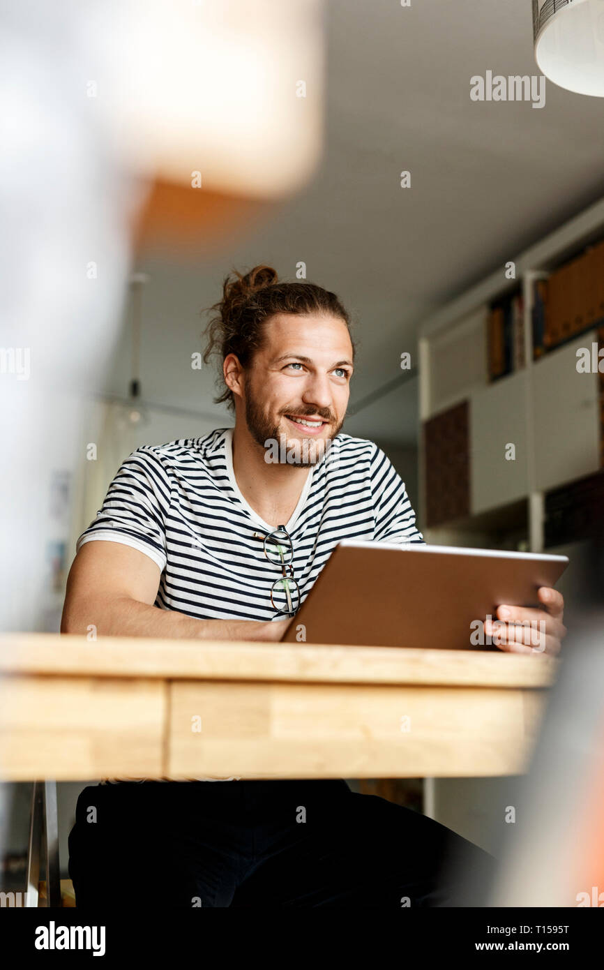 Young man with a bun sitting at home, using tablet Stock Photo