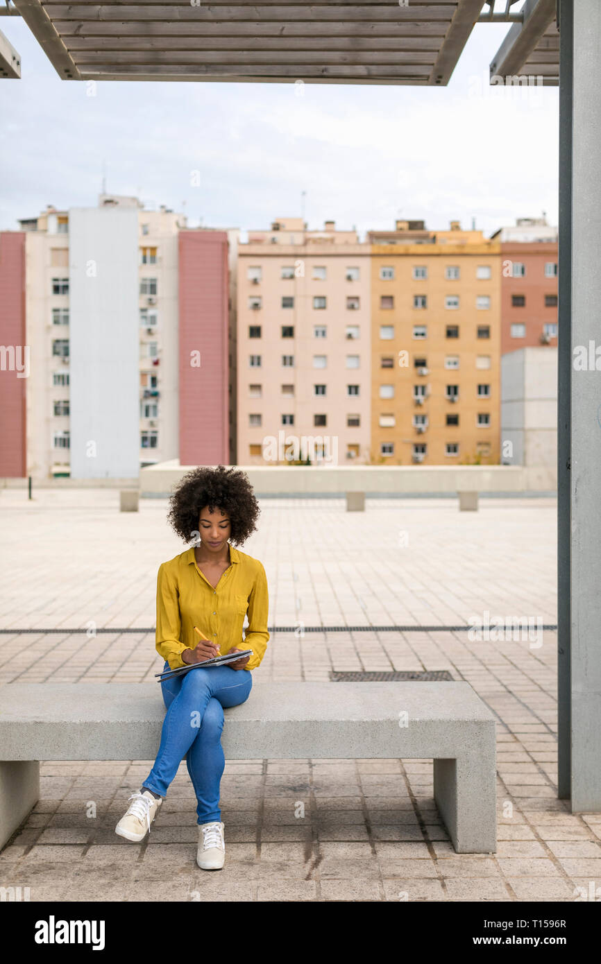 Woman sitting on bench taking notes Stock Photo