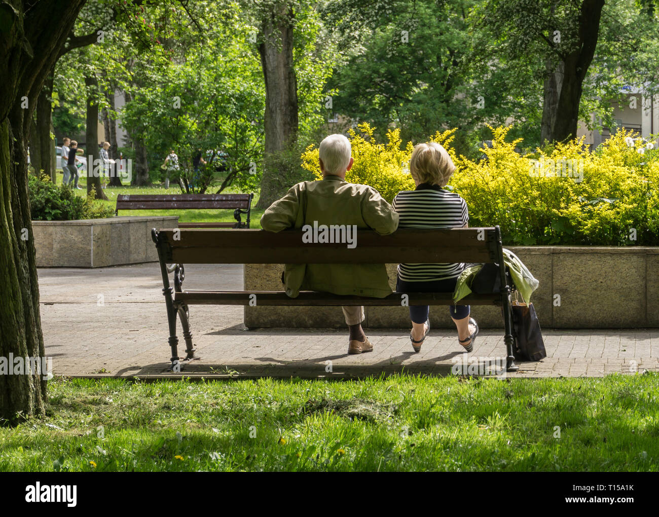 Mature couple sitting on a park bench and watching children playing. Stock Photo