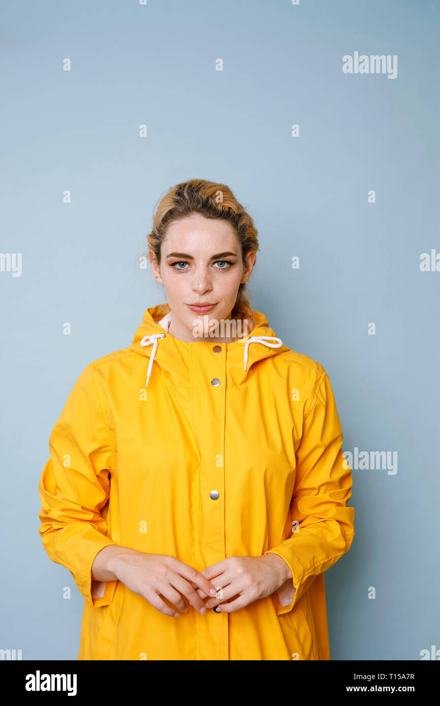 Portrait of young woman wearing yellow rain coat in front of blue ...