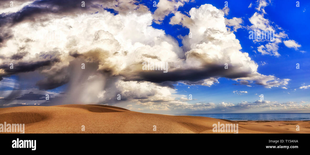 Structured and layered clouds over sand dunes of Stockton beach in Australia with strong storm raining down on earth from blue skies. Stock Photo