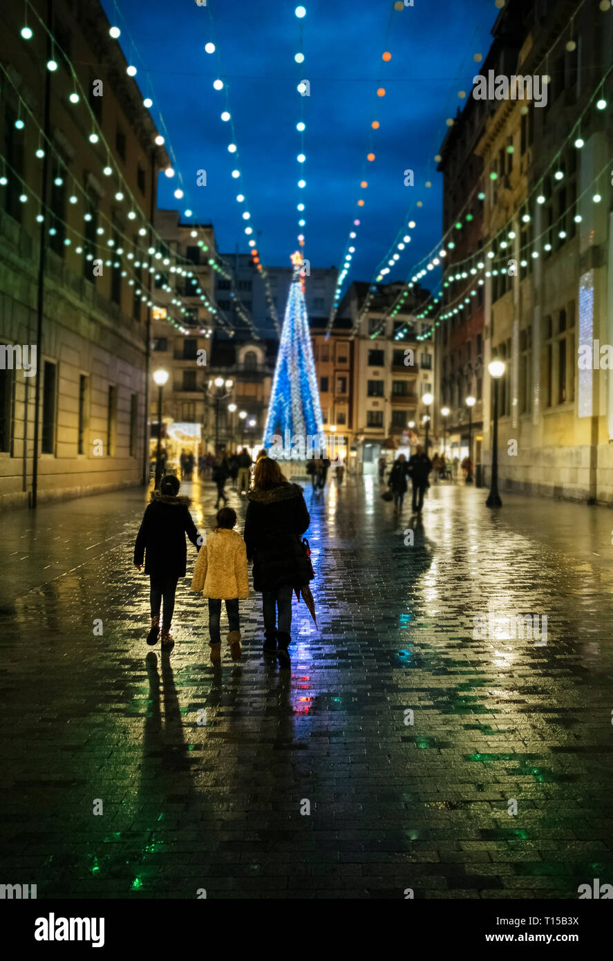 Spain, Gijon, back view of mother and two children walking at pedestrian area in the evening at Christmas time Stock Photo