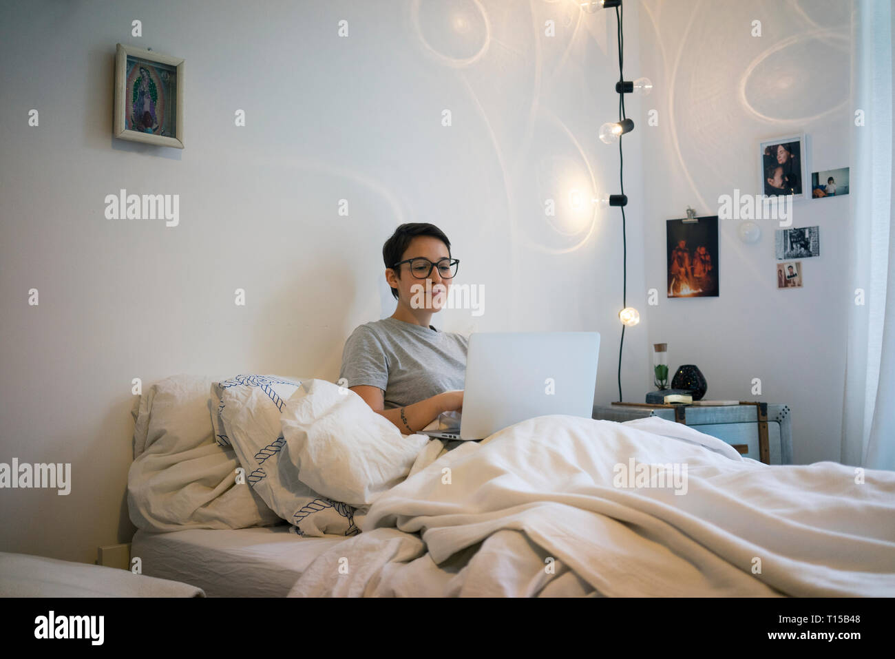 Young woman sitting in bed, using laptop Stock Photo