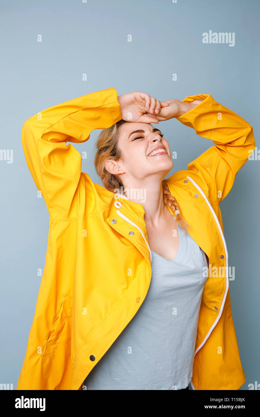 Happy young woman wearing yellow rain coat in front of blue background ...