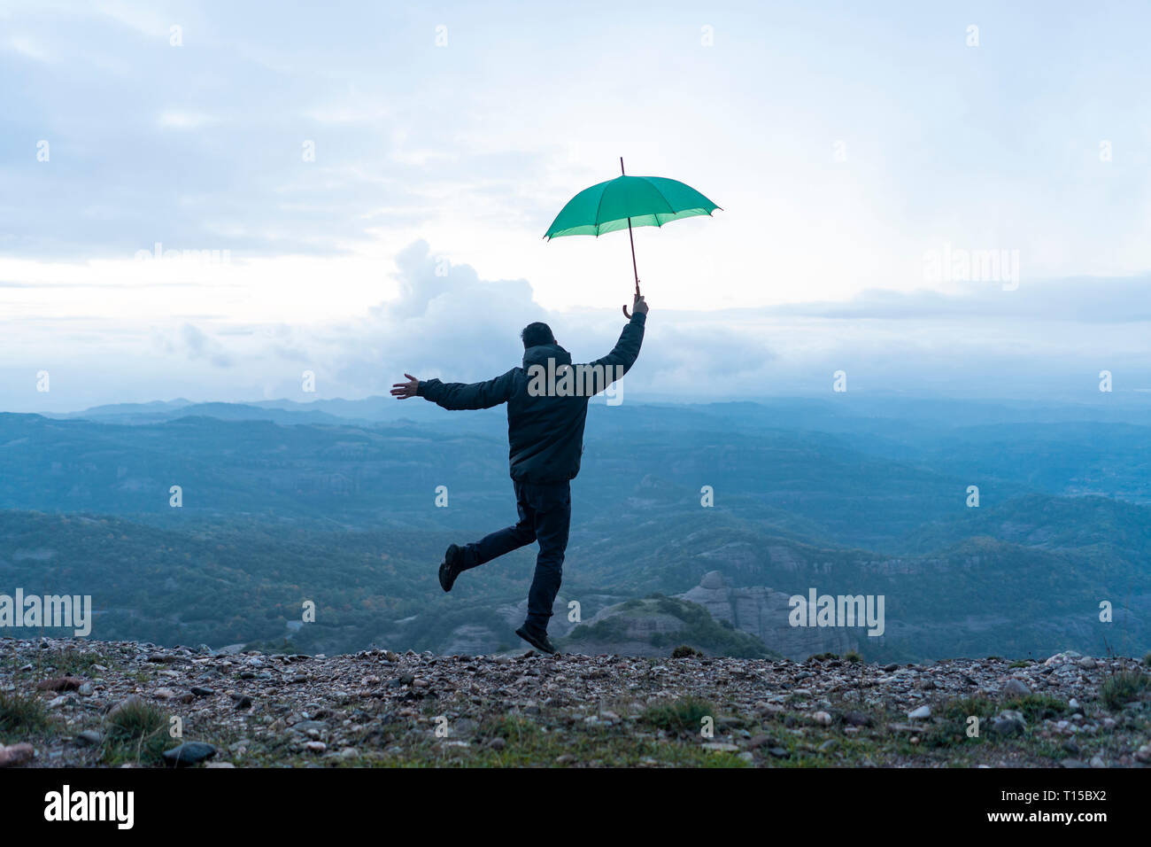 Man jumping for joy on a mountain, holding a green umbrella Stock Photo