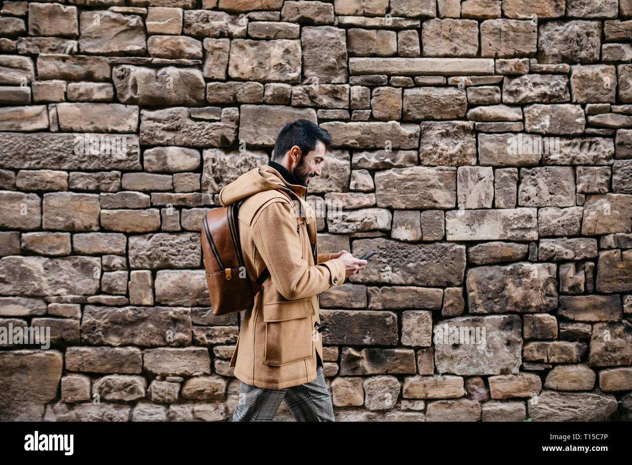Spain, Igualada, man walking along stone wall using cell phone Stock Photo