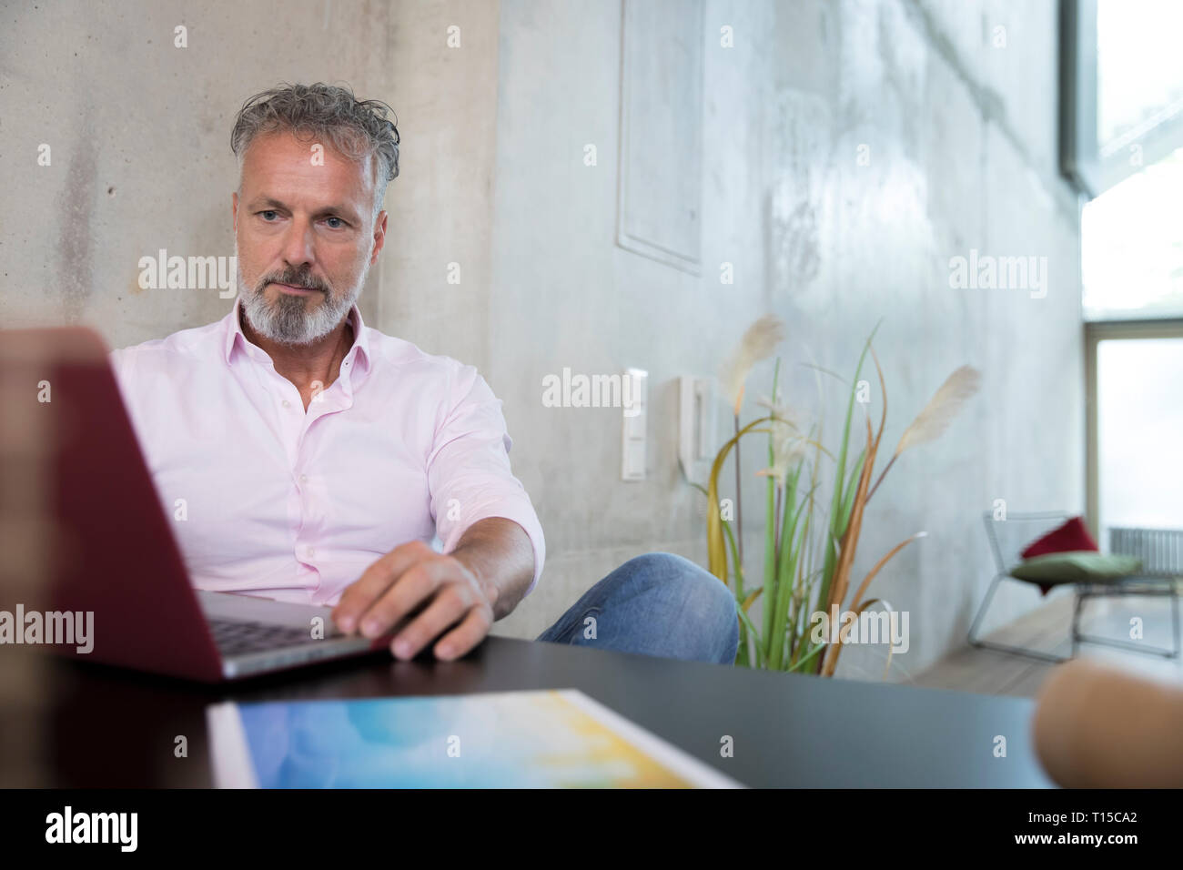 Businessman sitting at table in a loft using laptop Stock Photo
