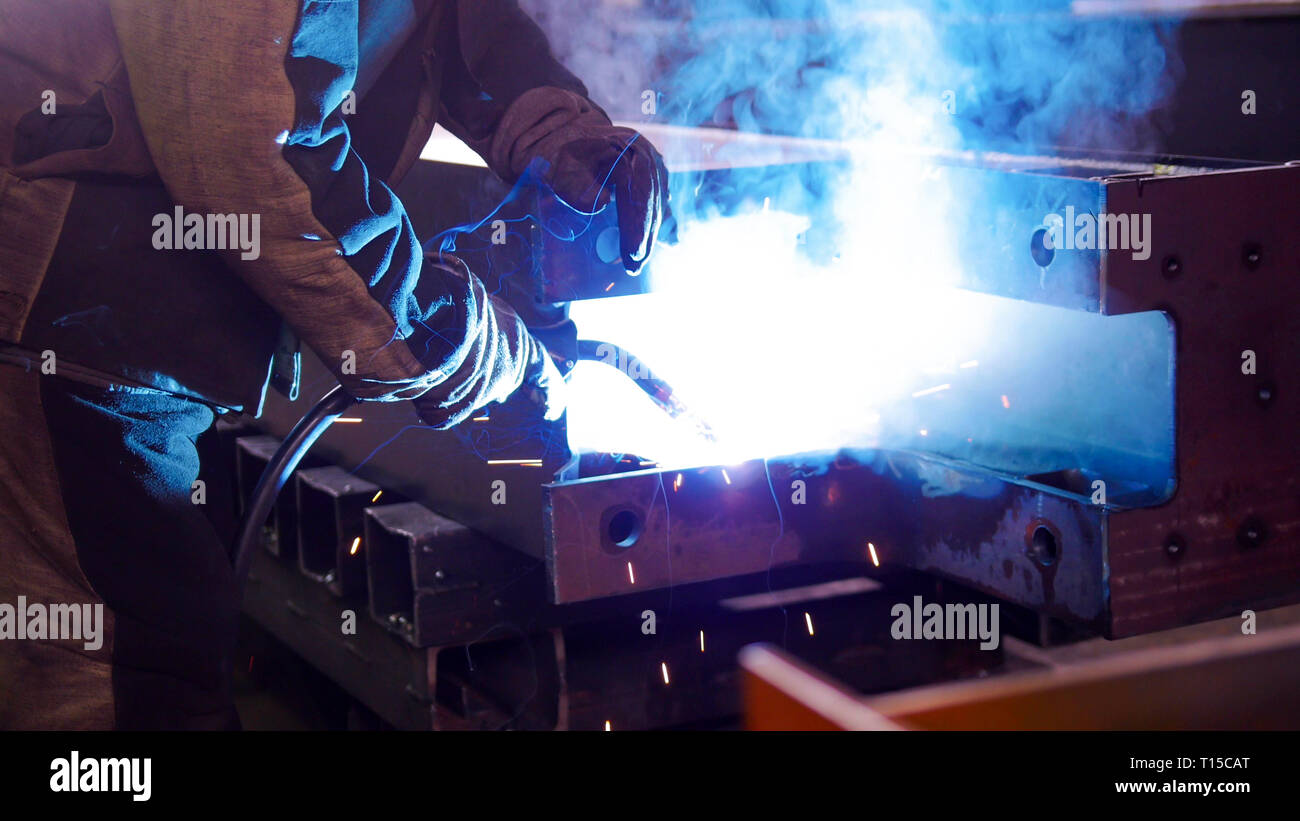 A man at the construction plant using a welding machine. Bright blue lighting Stock Photo