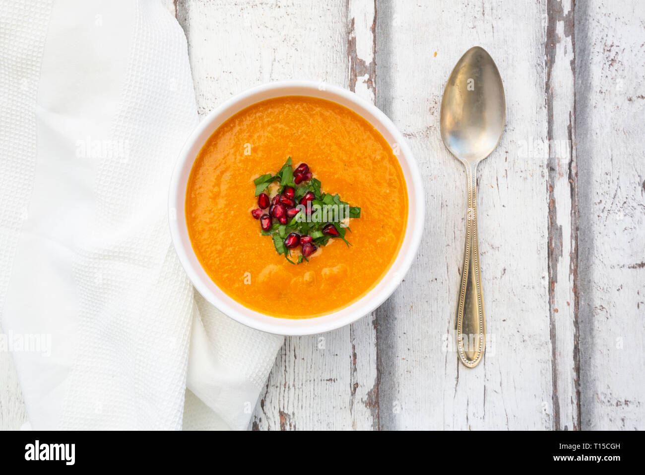 Bowl of carrot ginger coconut soup with topping of parsley and pomegranate seed Stock Photo