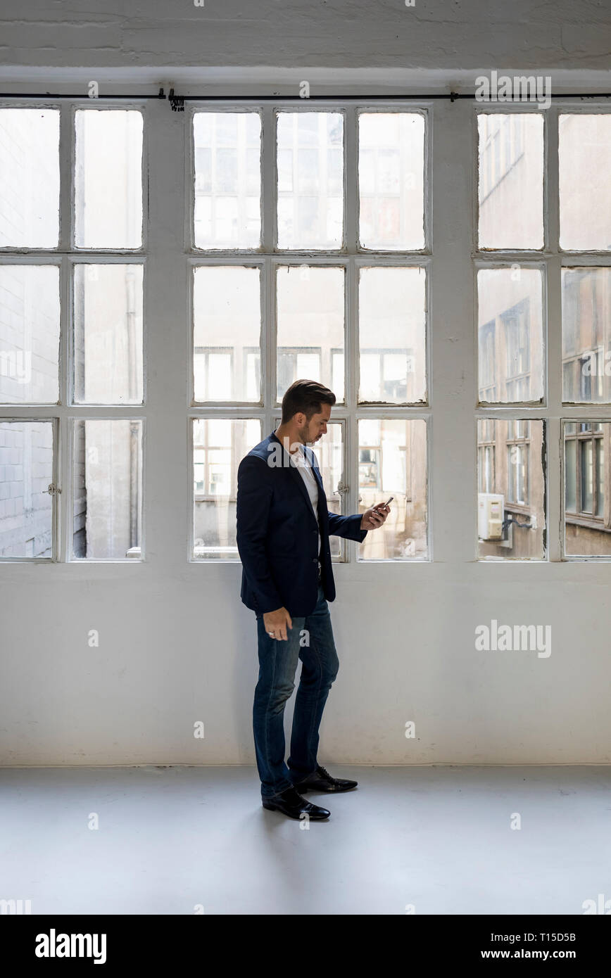 Businessman standing in a loft at the window using cell phone Stock Photo