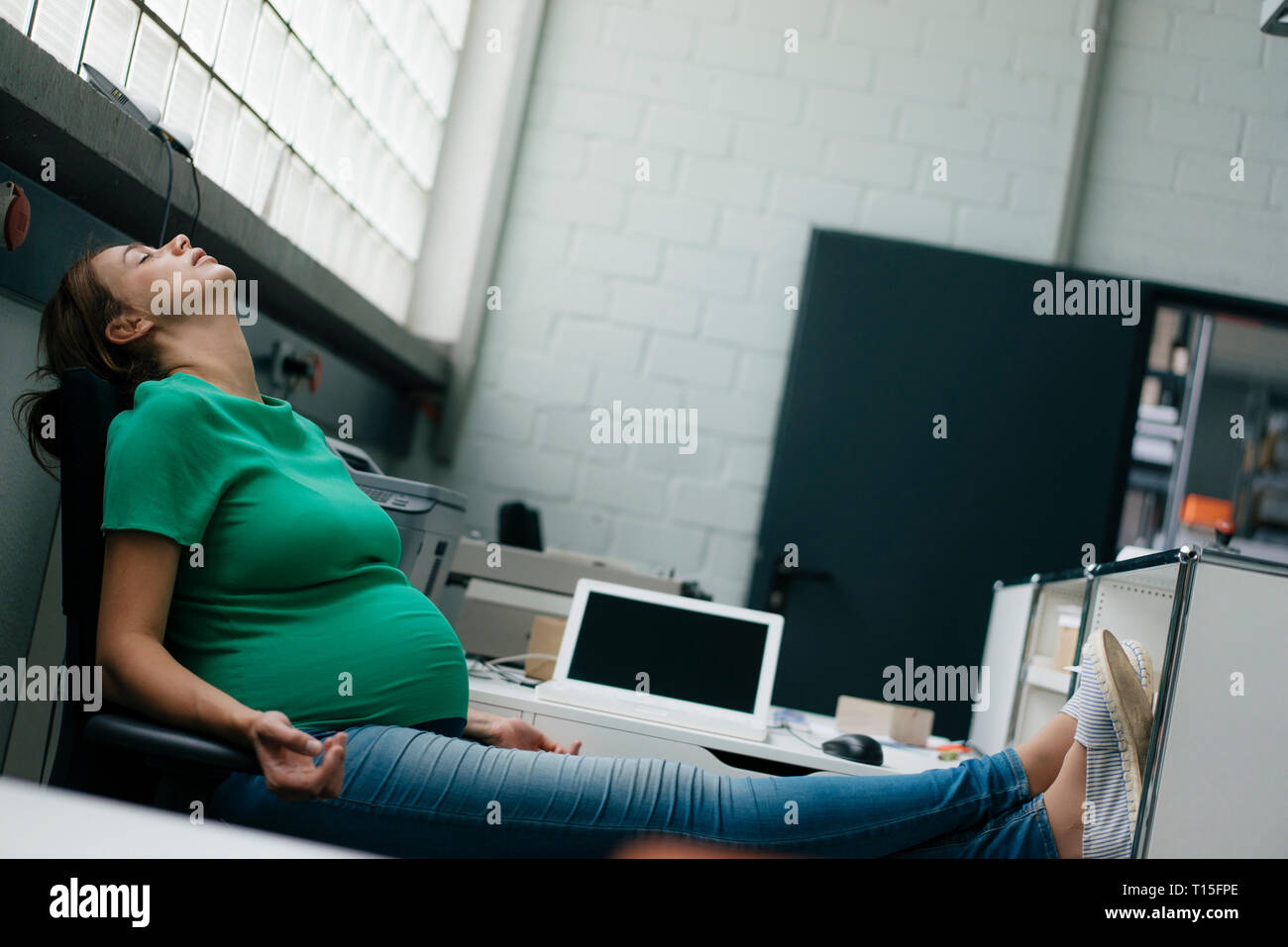 Exhausted pregnant woman sitting at desk in office having a break Stock