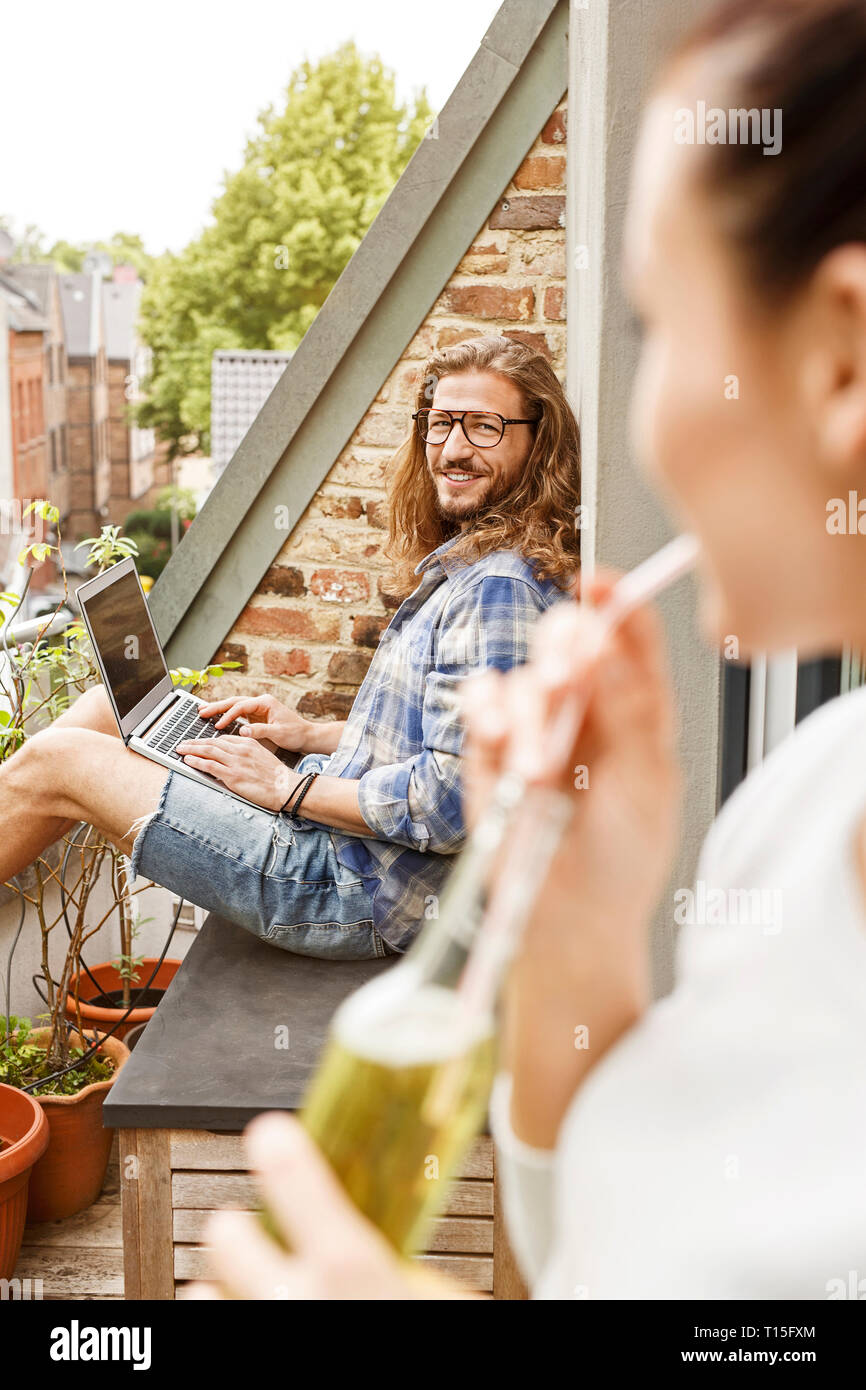 Young couple sitting on their balcony in summer, man using laptop Stock Photo