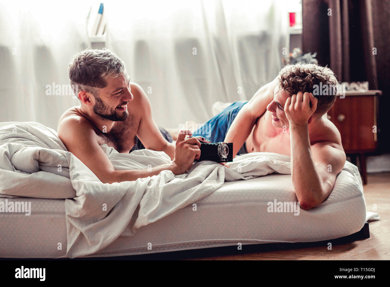 Happy gay couple with old-fashioned camera in bed Stock Photo - Alamy