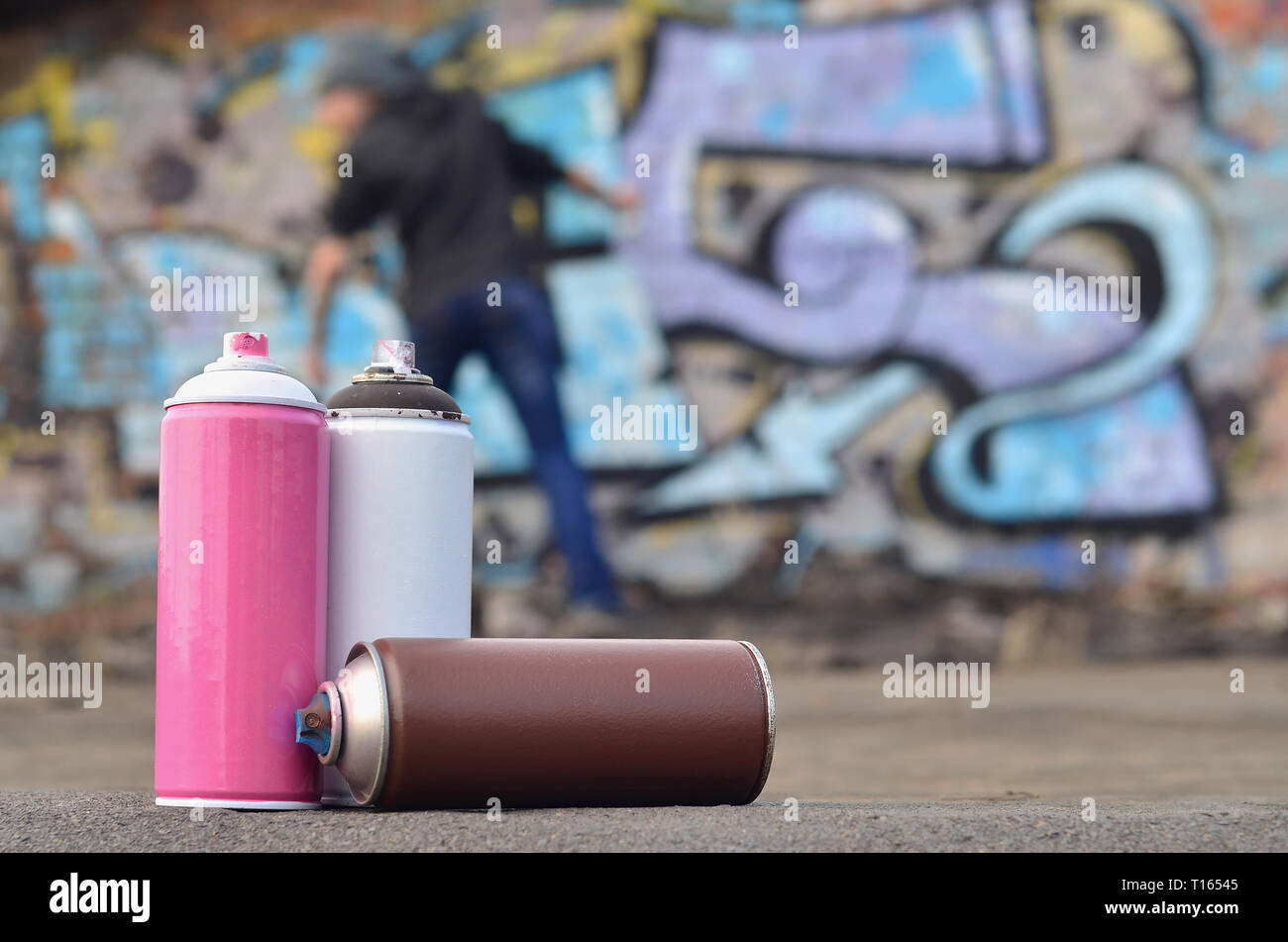 A photography of a certain number of paint cans against the background of the space with the wall on which the young guy draws a large graffiti drawin Stock Photo