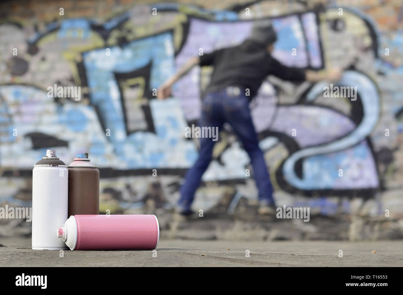 A photography of a certain number of paint cans against the background of the space with the wall on which the young guy draws a large graffiti drawin Stock Photo