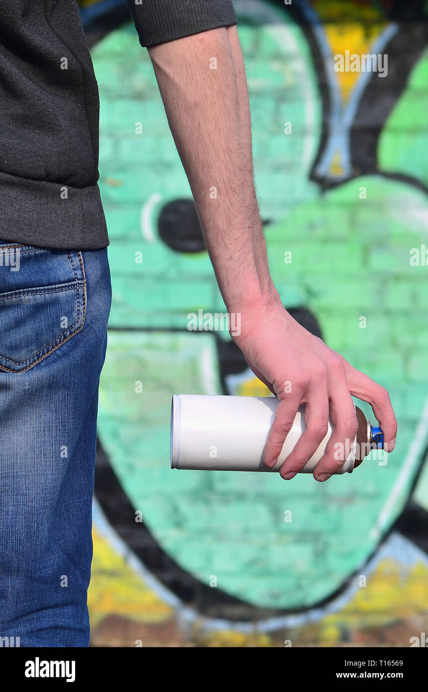 A photo of a bully who spoils state property, paints walls with aerosol paint. Fragment of the body of a young criminal vandal with a paint sprayer in Stock Photo