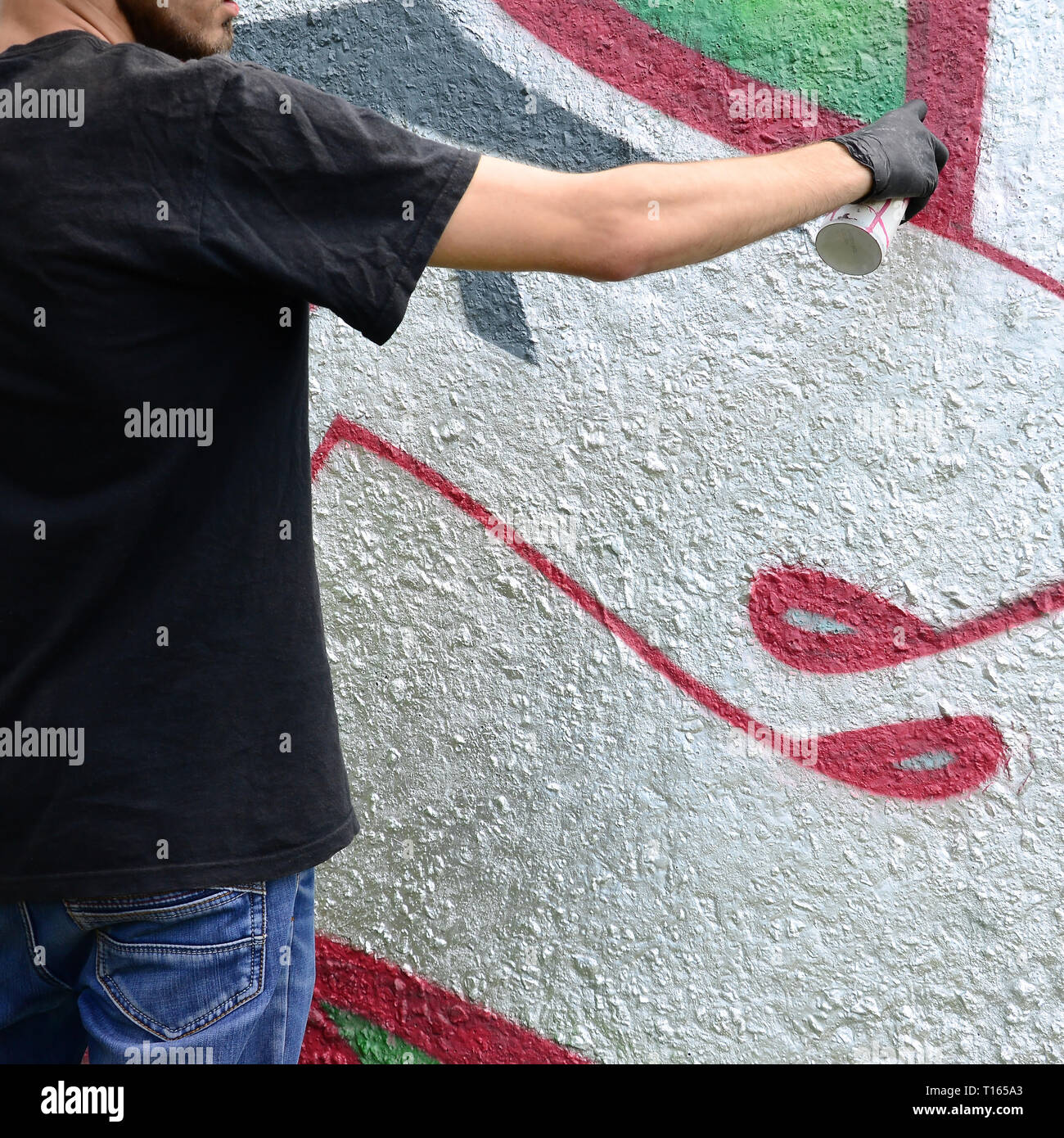 A young hooligan paints graffiti on a concrete wall. Illegal vandalism concept. Street art. Stock Photo