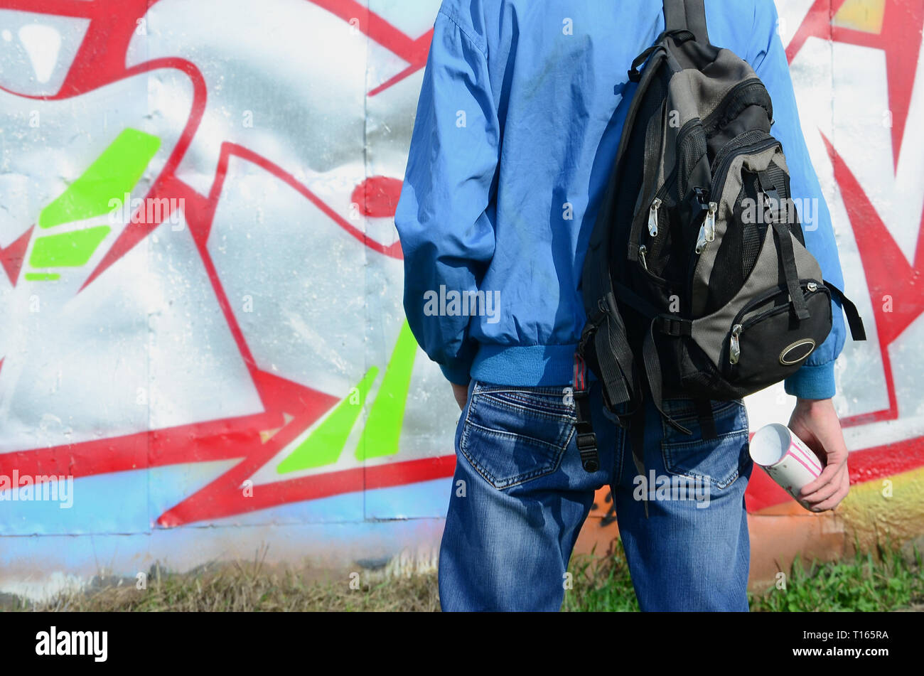 A young graffiti artist with a black bag looks at the wall with his ...