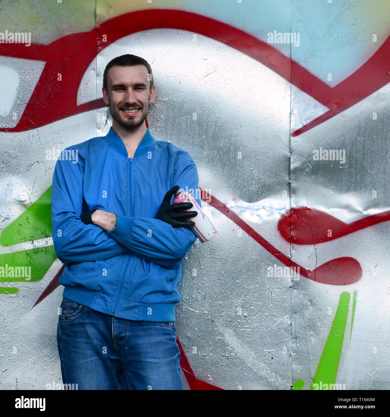 The graffiti artist with spray can poses against the background of a ...