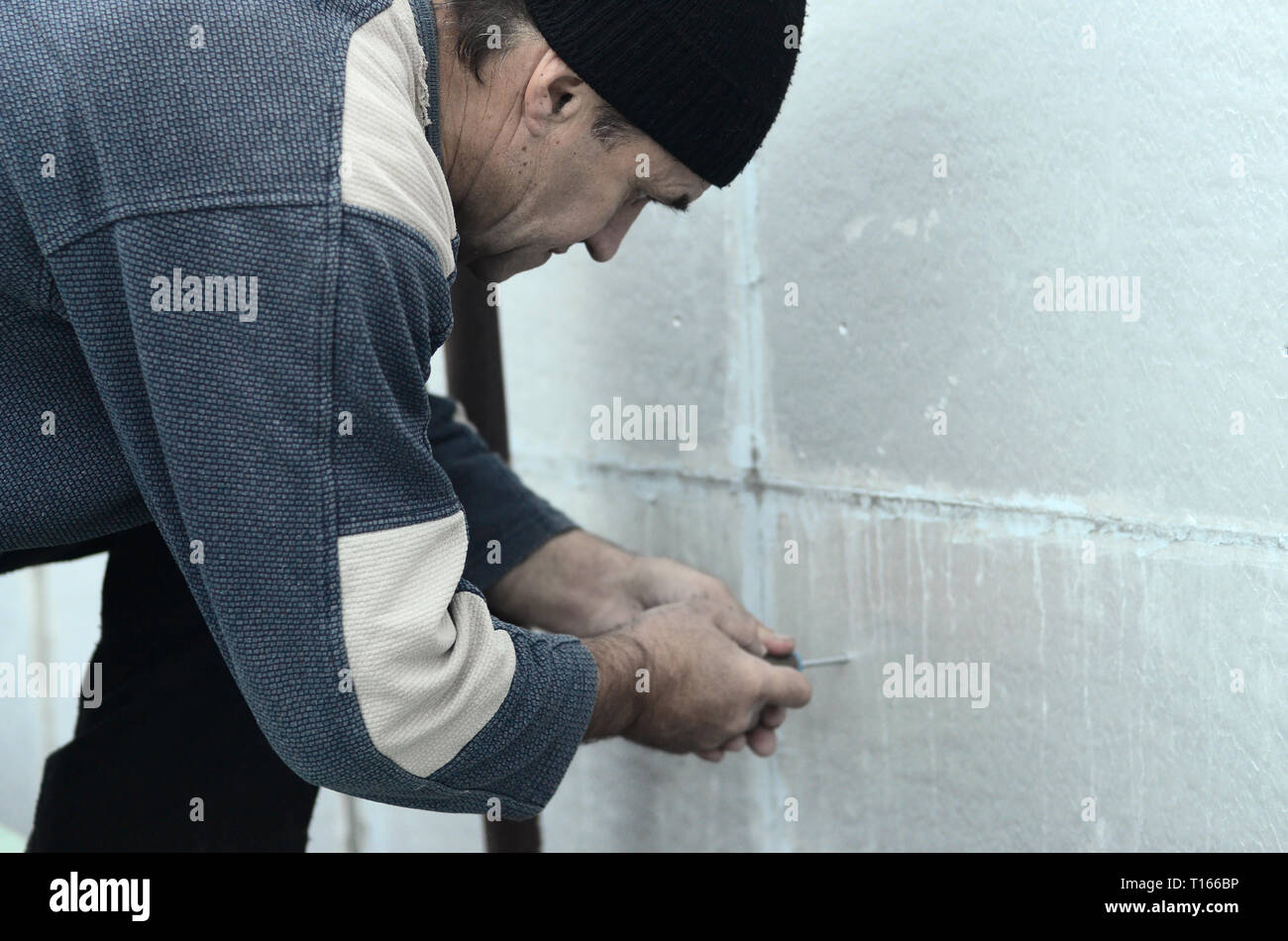 An elderly worker creates holes in the expanded polystyrene wall for