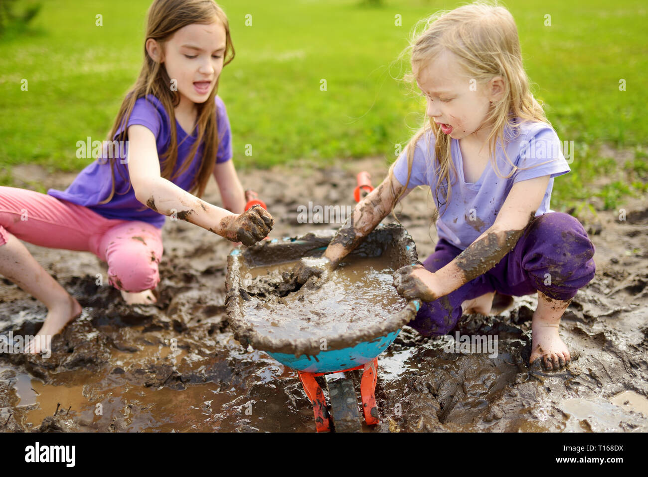 Two funny little girls playing in a large wet mud puddle on sunny