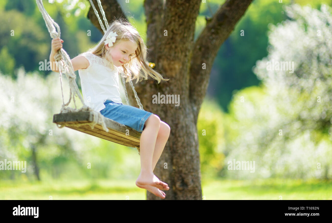 Cute little girl having fun on a swing in blossoming old apple tree ...